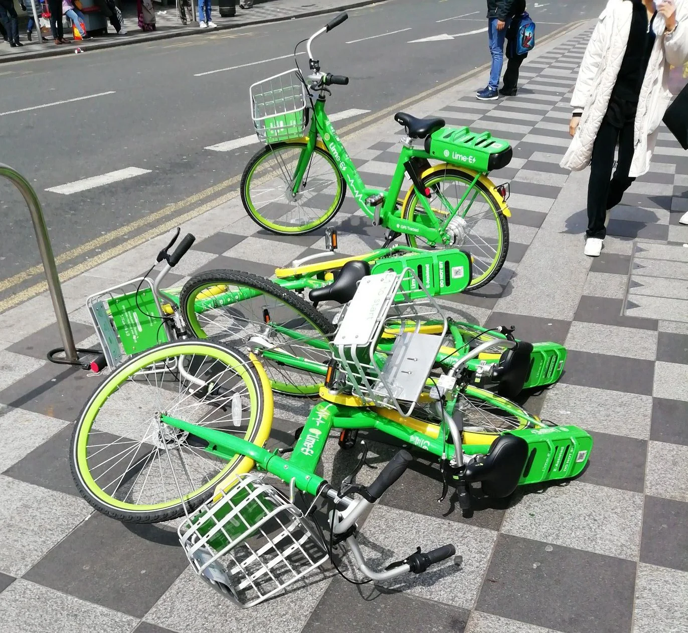 Chaotic pile of discarded commercial dockless bicycles dumped across a public pedestrian pavement